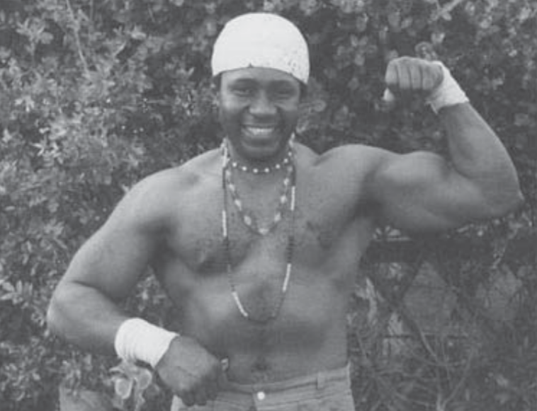 Mama Herc smiling and flexing his arm in a black-and-white photograph